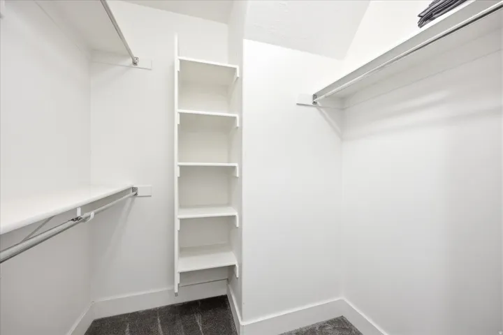 Walk-in closet featuring built-in shelving, white walls, and dark carpeting