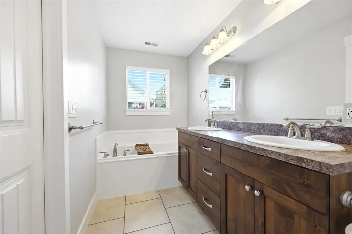 Bathroom featuring a dual vanity with a dark wood-finish cabinet, a full-width mirror, and a built-in soaking tub