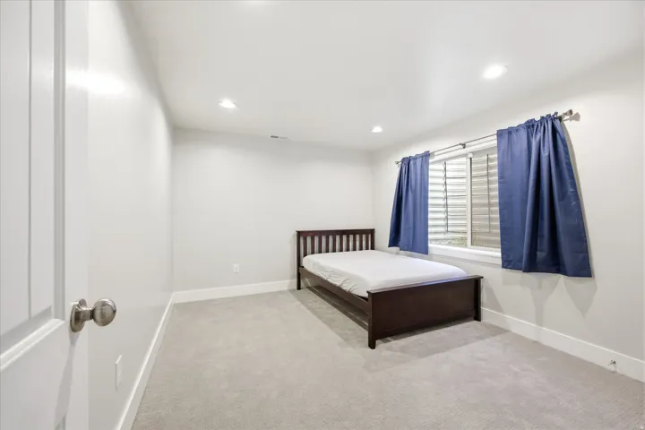Recessed lighting illuminates this room, featuring light gray carpeting and white baseboards
