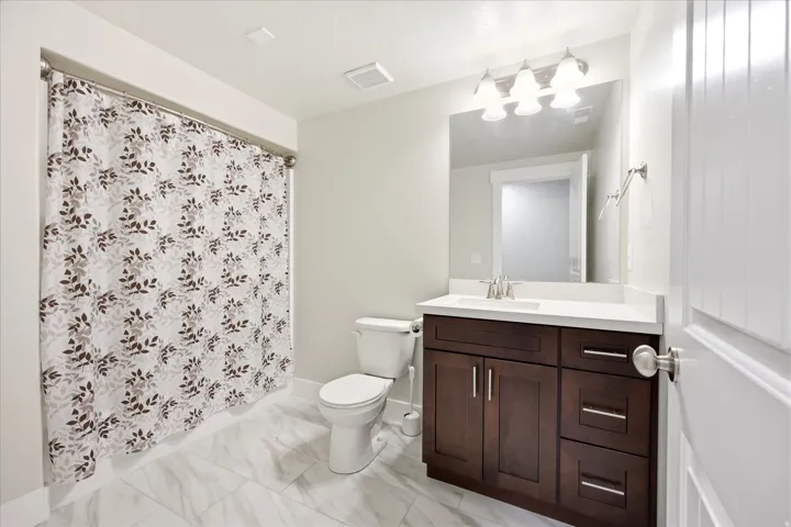 Bathroom featuring a dark wood-finish vanity with a white countertop and rectangular sink, a wall-mounted mirror with overhead lighting, and large format white tile flooring