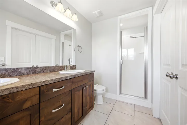 Double vanity with wood-finish cabinetry and undermount sinks, set under a large mirror with a three-light fixture