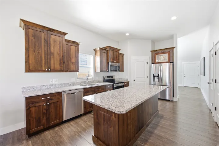 Spacious kitchen featuring an expansive center island, wood-finish flooring, dark wood cabinetry, granite countertops, and stainless steel appliances