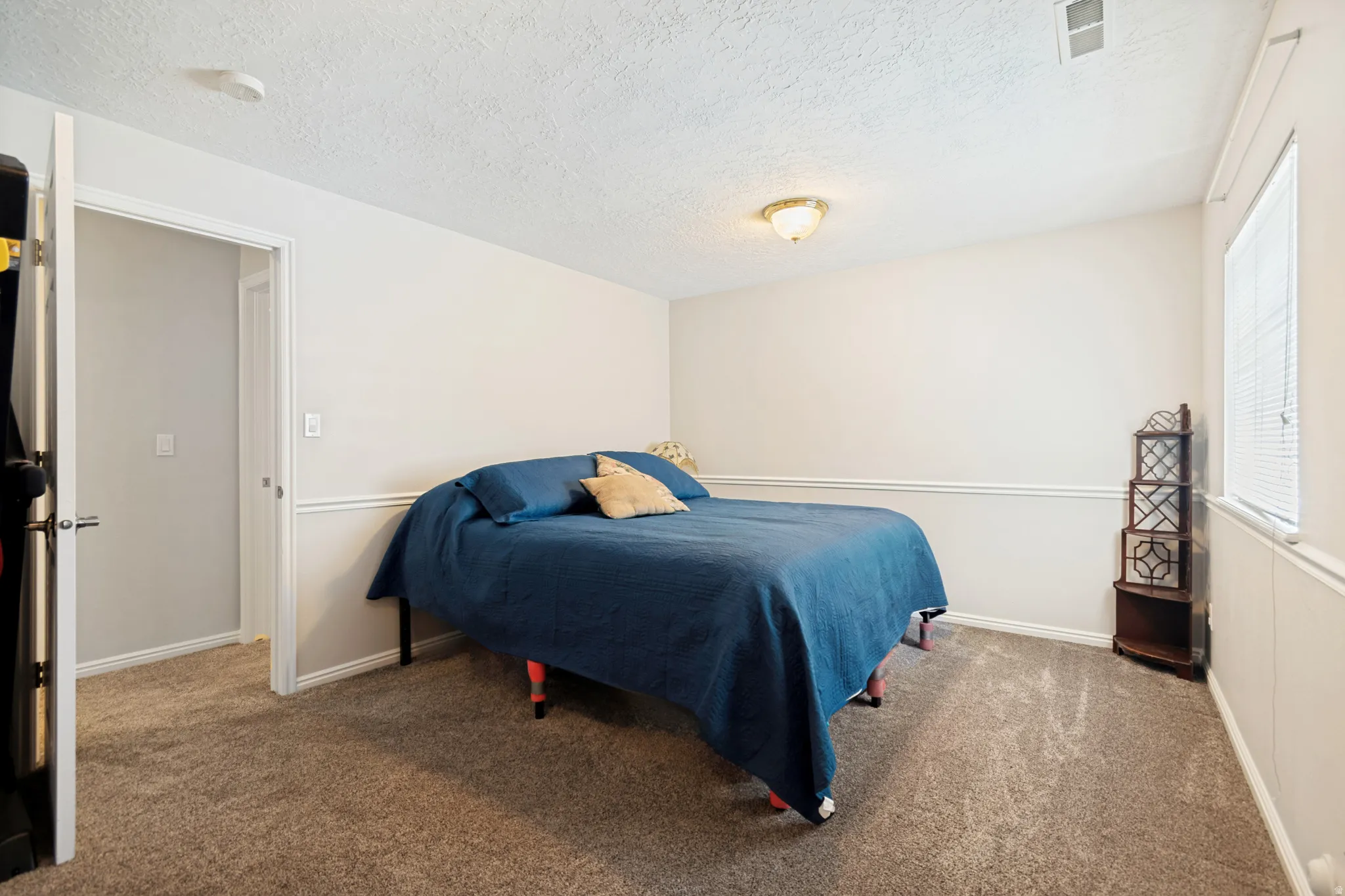 Carpeted room featuring a ceiling-mounted light fixture, white trim, and a window with blinds