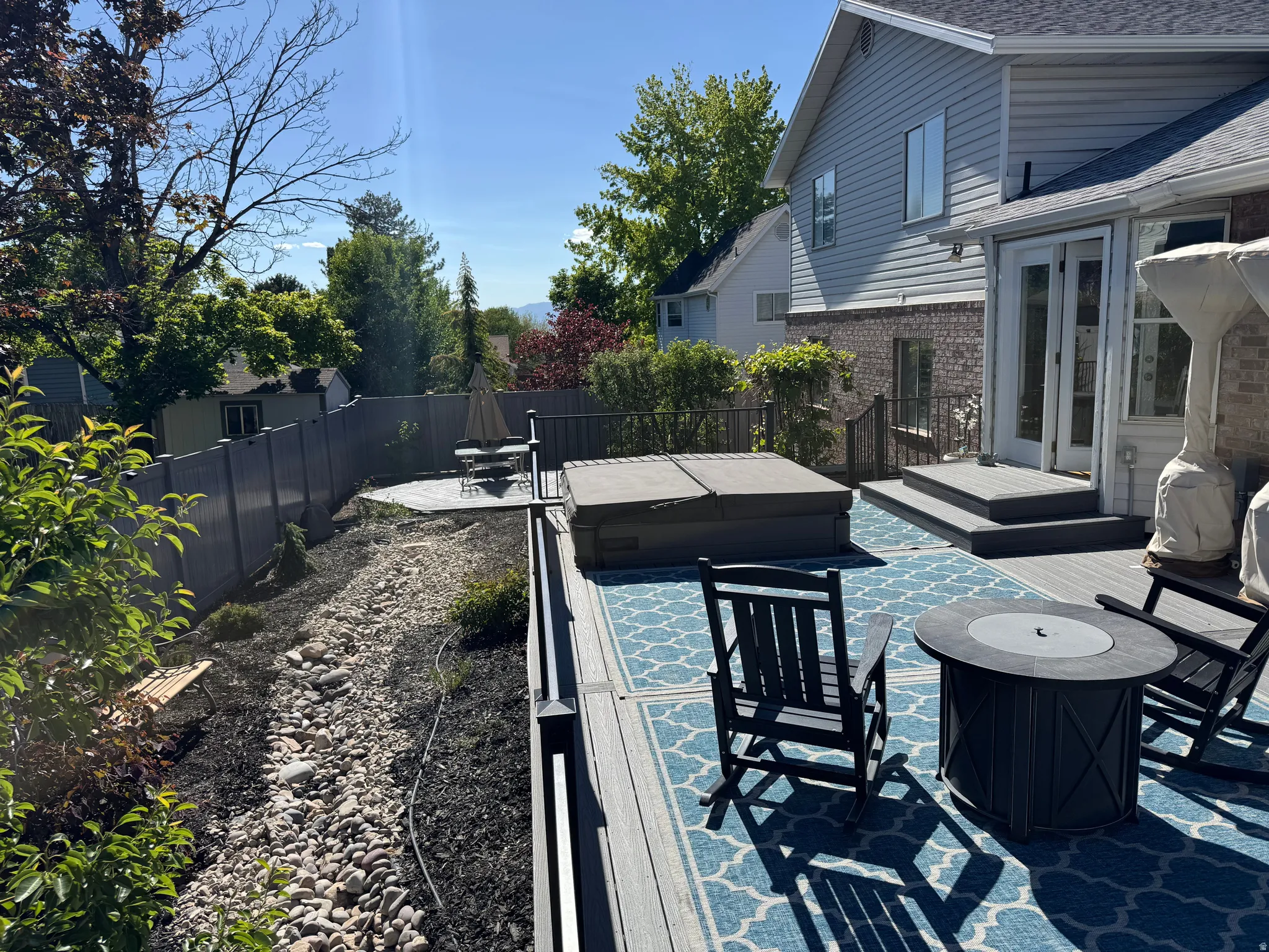 NOTE STREAM WATER FEATURE (On left hand side of photo):Spacious multi-level deck featuring a built-in hot tub, direct access to the interior via French doors, and a decorative rock bed with dark mulch along the property line.  Hot Tub is new this year.