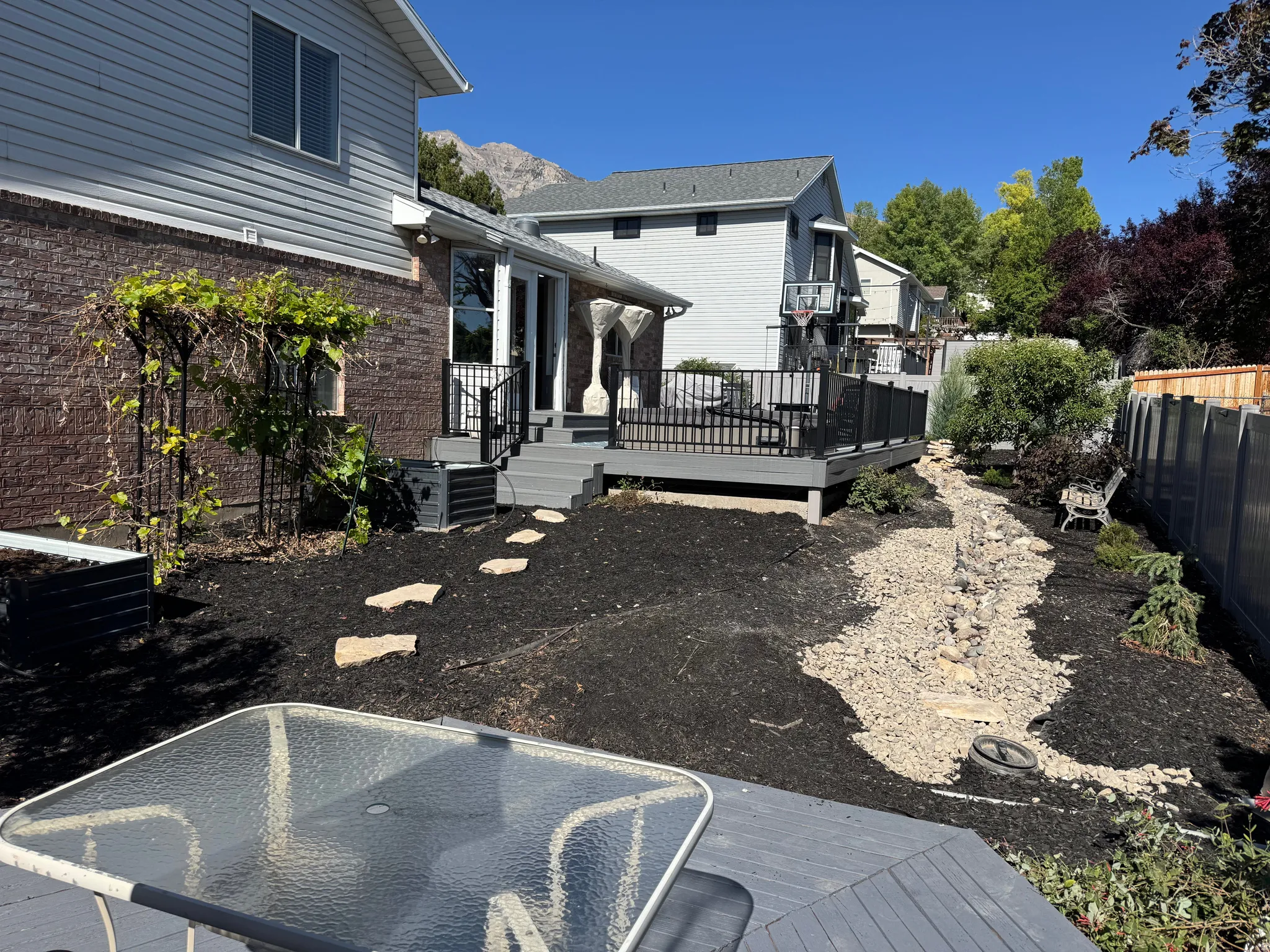 NOTE STREAM WATER FEATURE (On Right hand side of photo): Expansive backyard featuring a multi-level deck with black railing, a rock garden, and mature landscaping