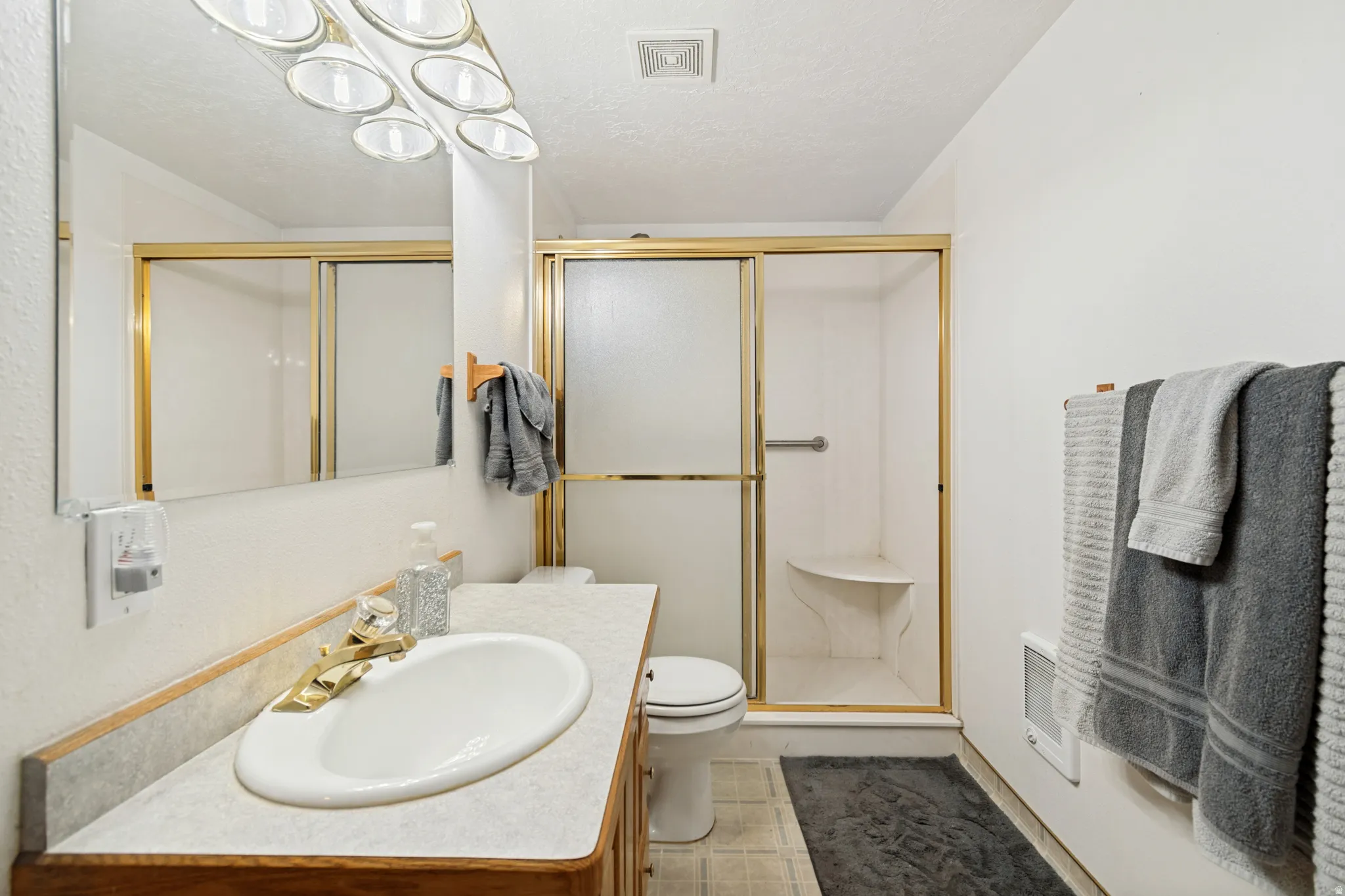 Bathroom featuring a vanity with an oval sink and gold-finish faucet, a large wall mirror, and a shower enclosure with gold-finish trim and a built-in seat
