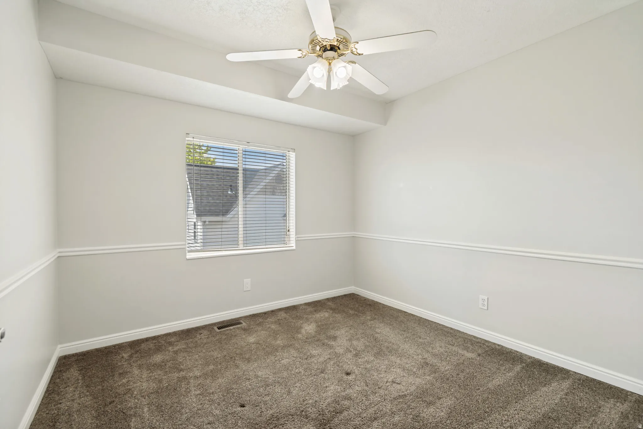 Light-filled room featuring neutral wall tones, textured carpeting, and a ceiling fan with integrated lighting