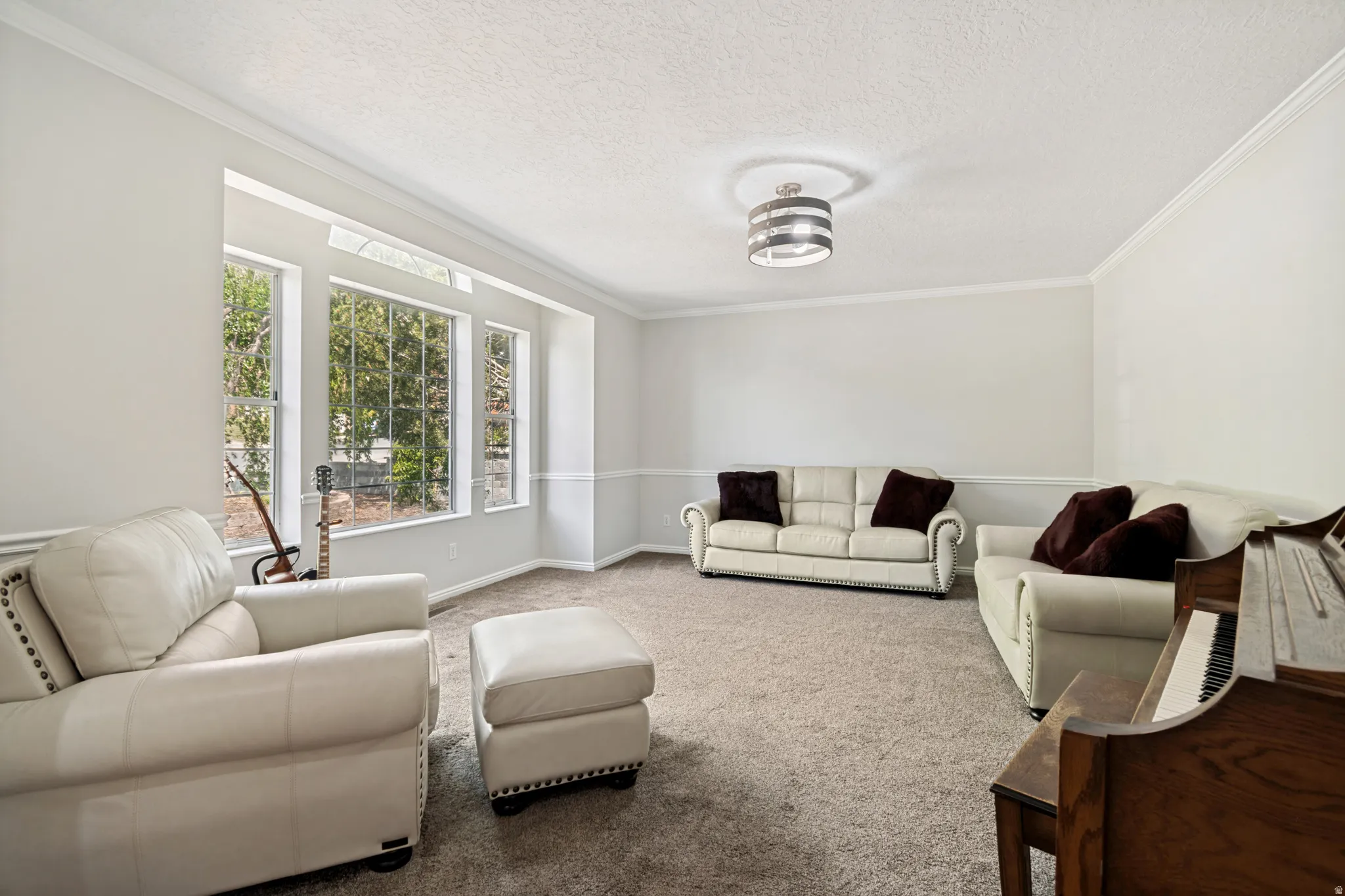 Spacious living area featuring neutral carpeting, a large bay window, crown molding, chair rail, and a contemporary ceiling light fixture