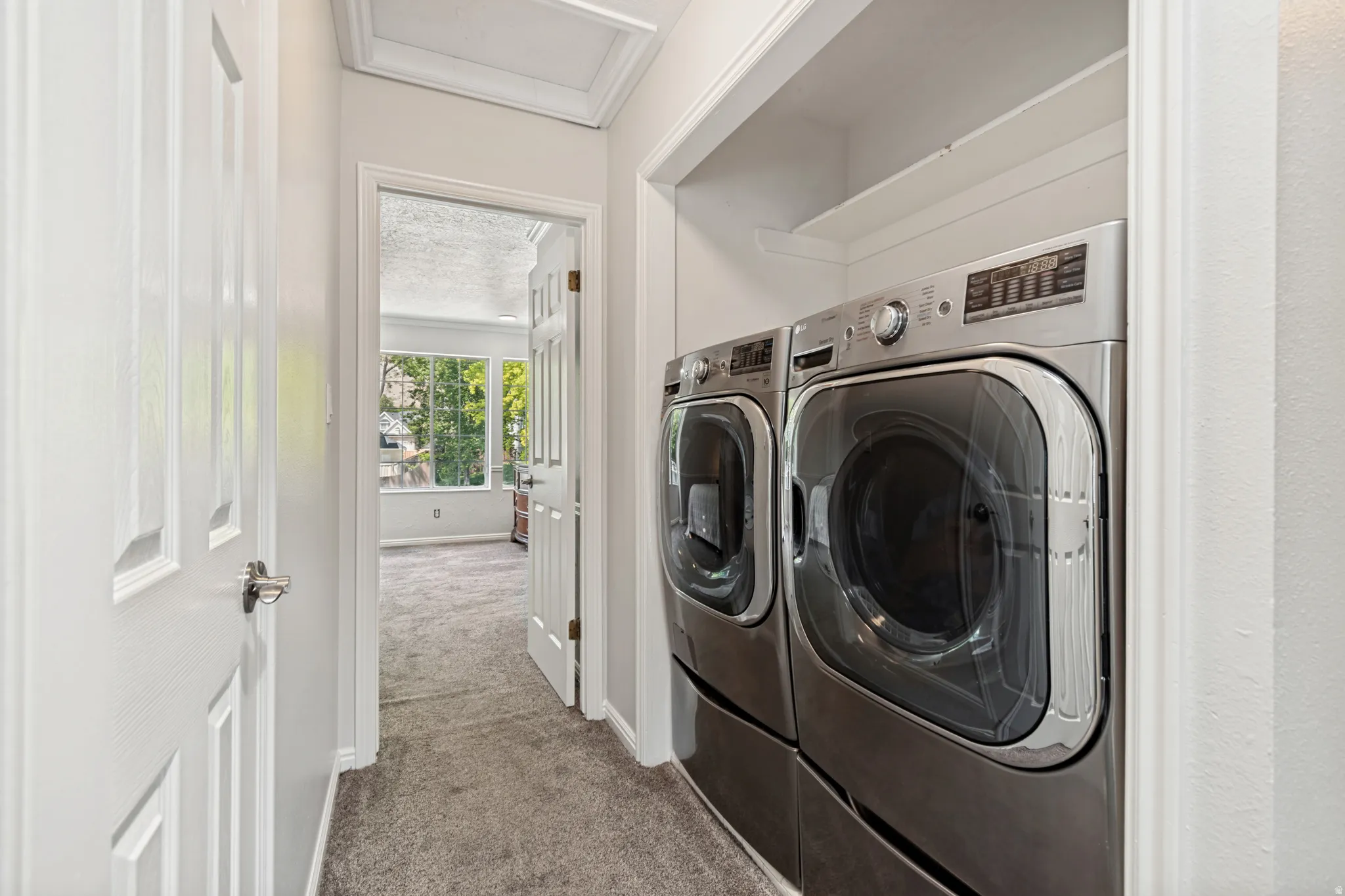 Dedicated laundry area featuring front-loading washer and dryer units, built-in shelving, paneled doors, and plush carpeting