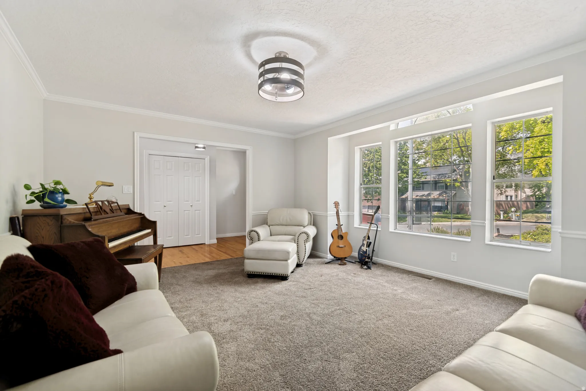 Spacious living area featuring expansive windows, neutral wall tones, textured carpeting, crown molding, and a contemporary ceiling fixture