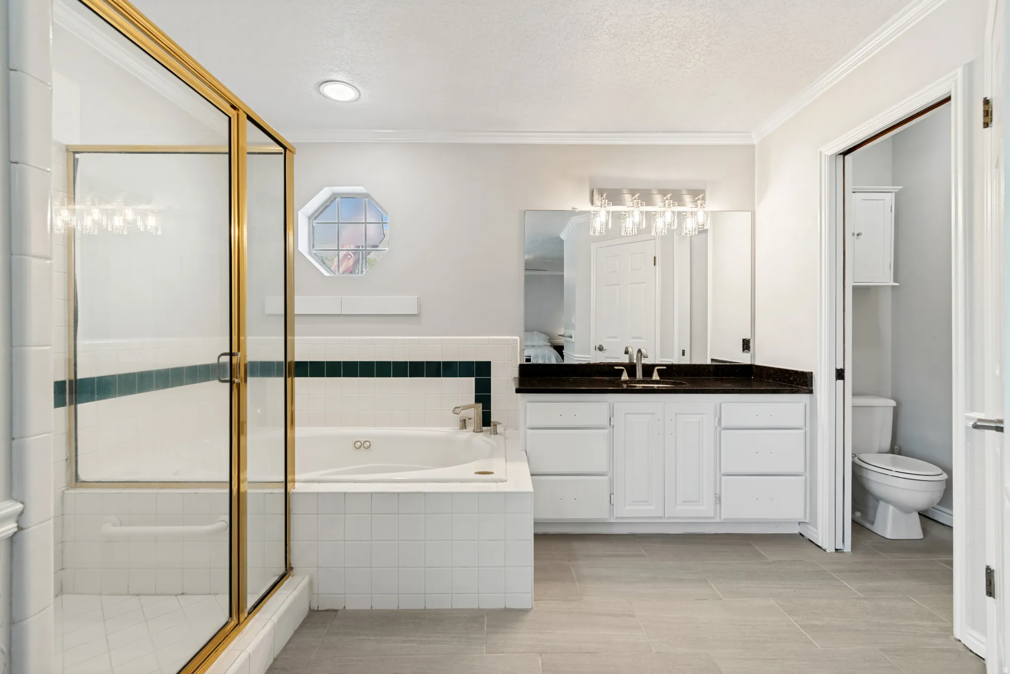 Primary Bathroom featuring a large soaking tub with tile surround, a separate shower with a gold-framed glass enclosure, and a vanity with white cabinetry and a dark countertop