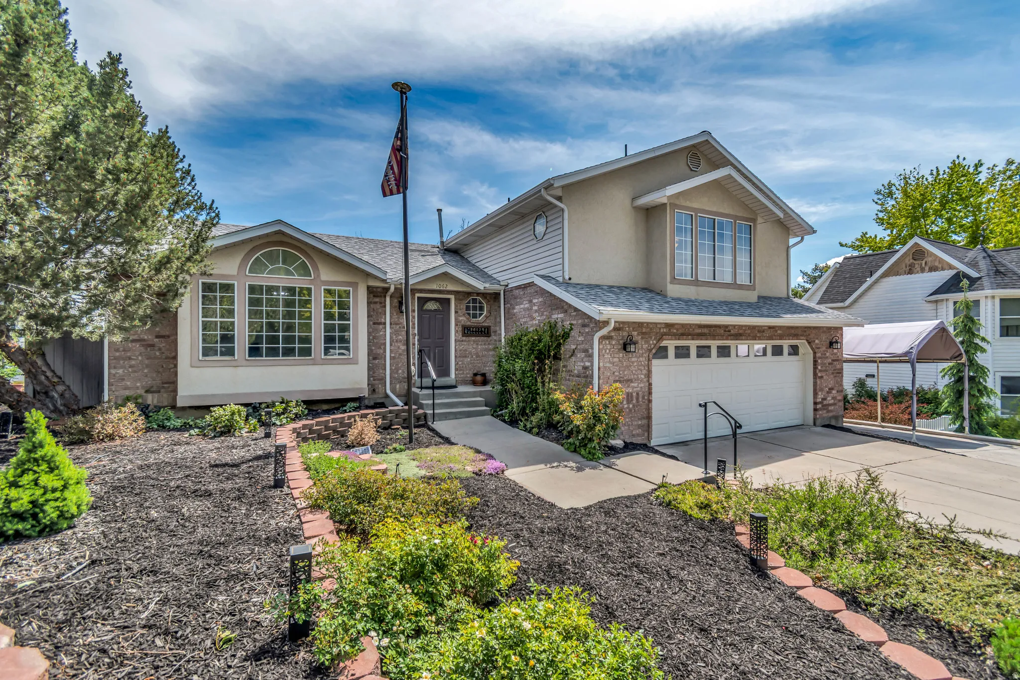 Multi-level residence featuring a brick and stucco exterior, an integrated two-car garage, and an arched bay window with muntin detailing