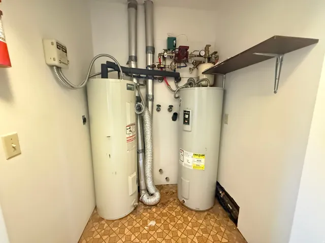 Utility closet featuring two water heaters, exposed piping, and a wall-mounted shelf