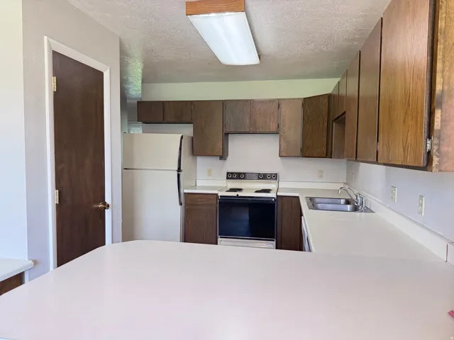 Kitchen featuring wood-finish cabinetry, white countertops, a stainless steel double-basin sink, and a white refrigerator