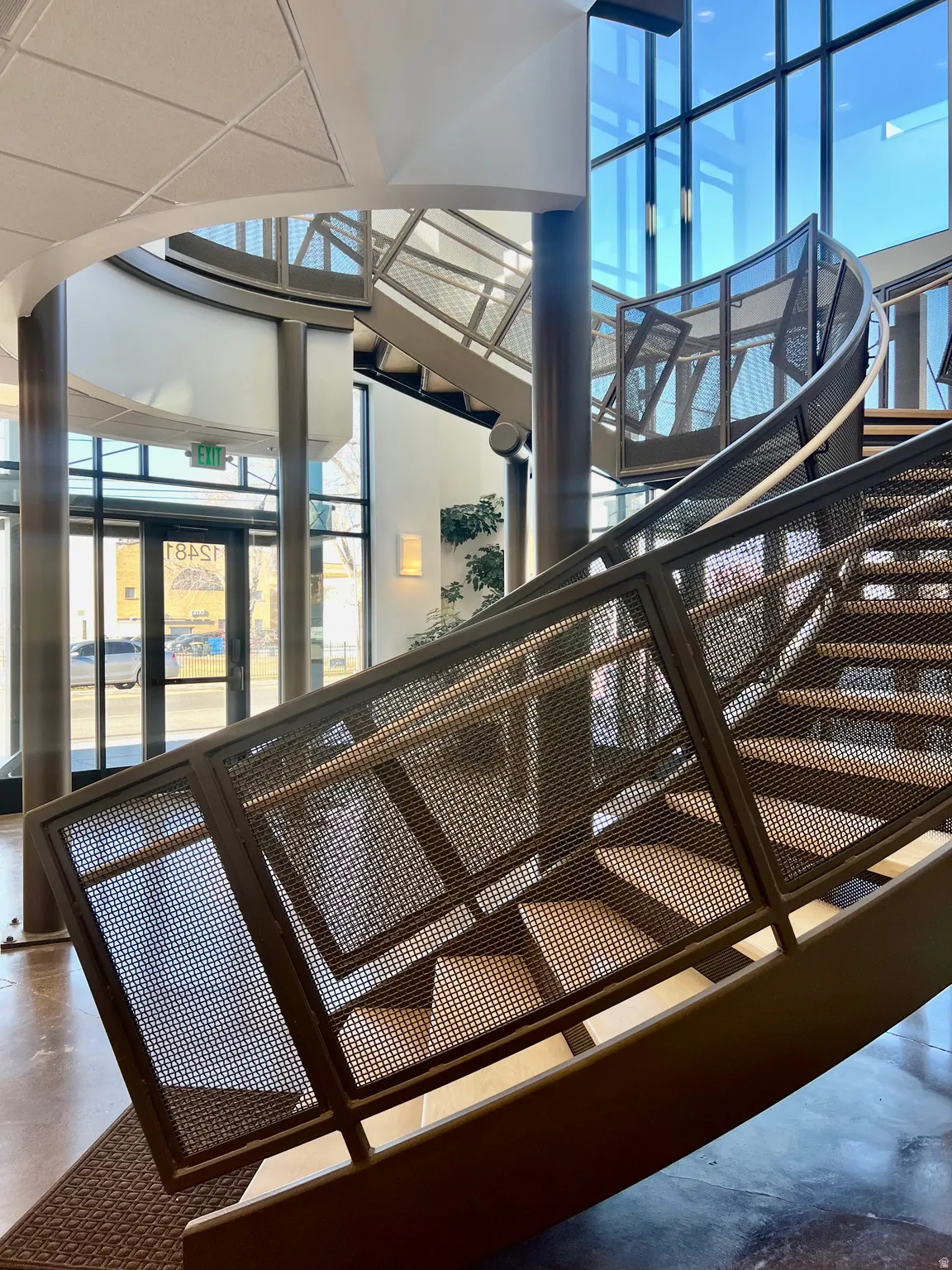 Modern spiral staircase featuring perforated metal railings, light wood-finish treads, and structural metal supports