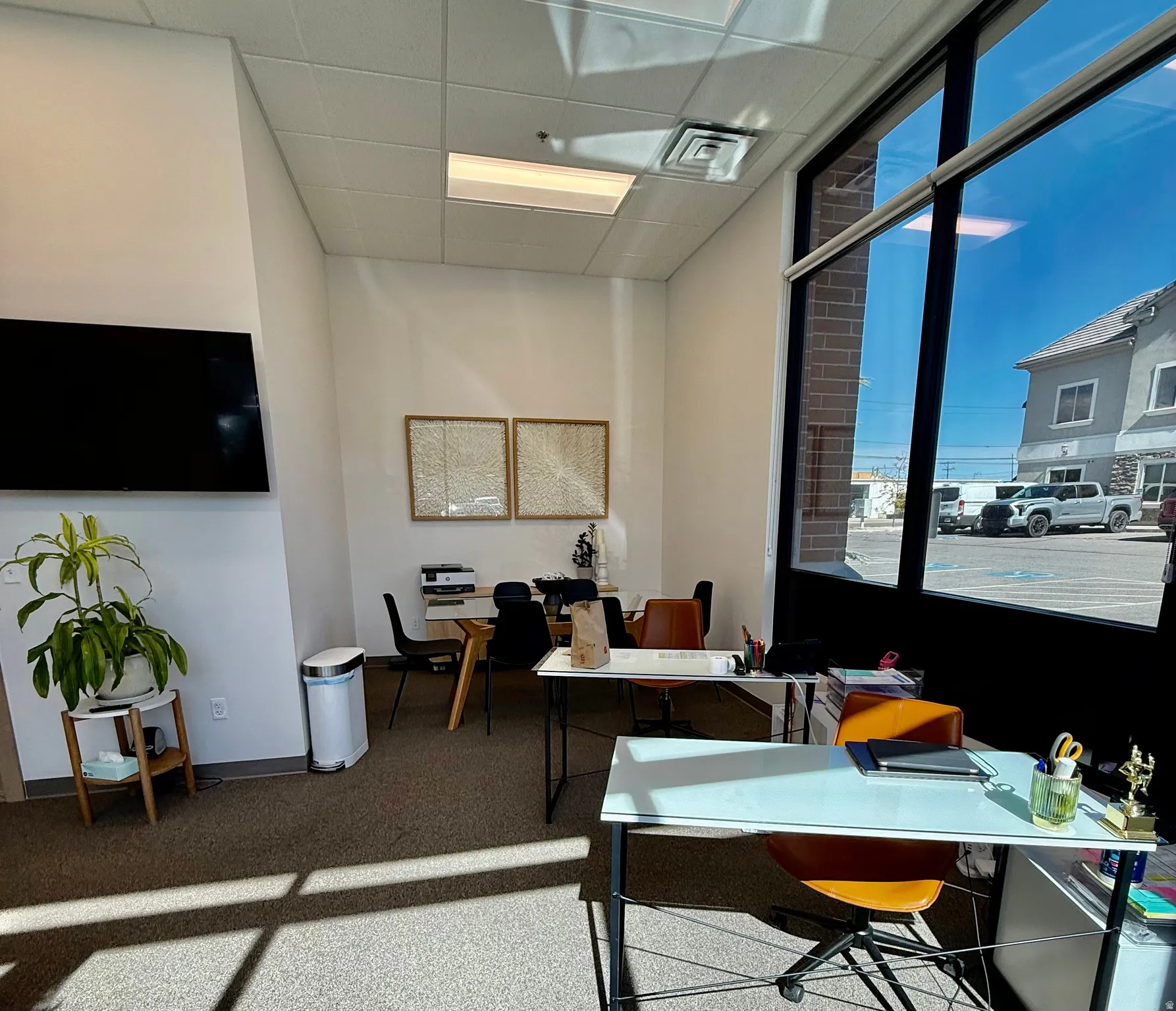 Open workspace featuring large windows, recessed ceiling lighting, a mounted display, and neutral carpeting