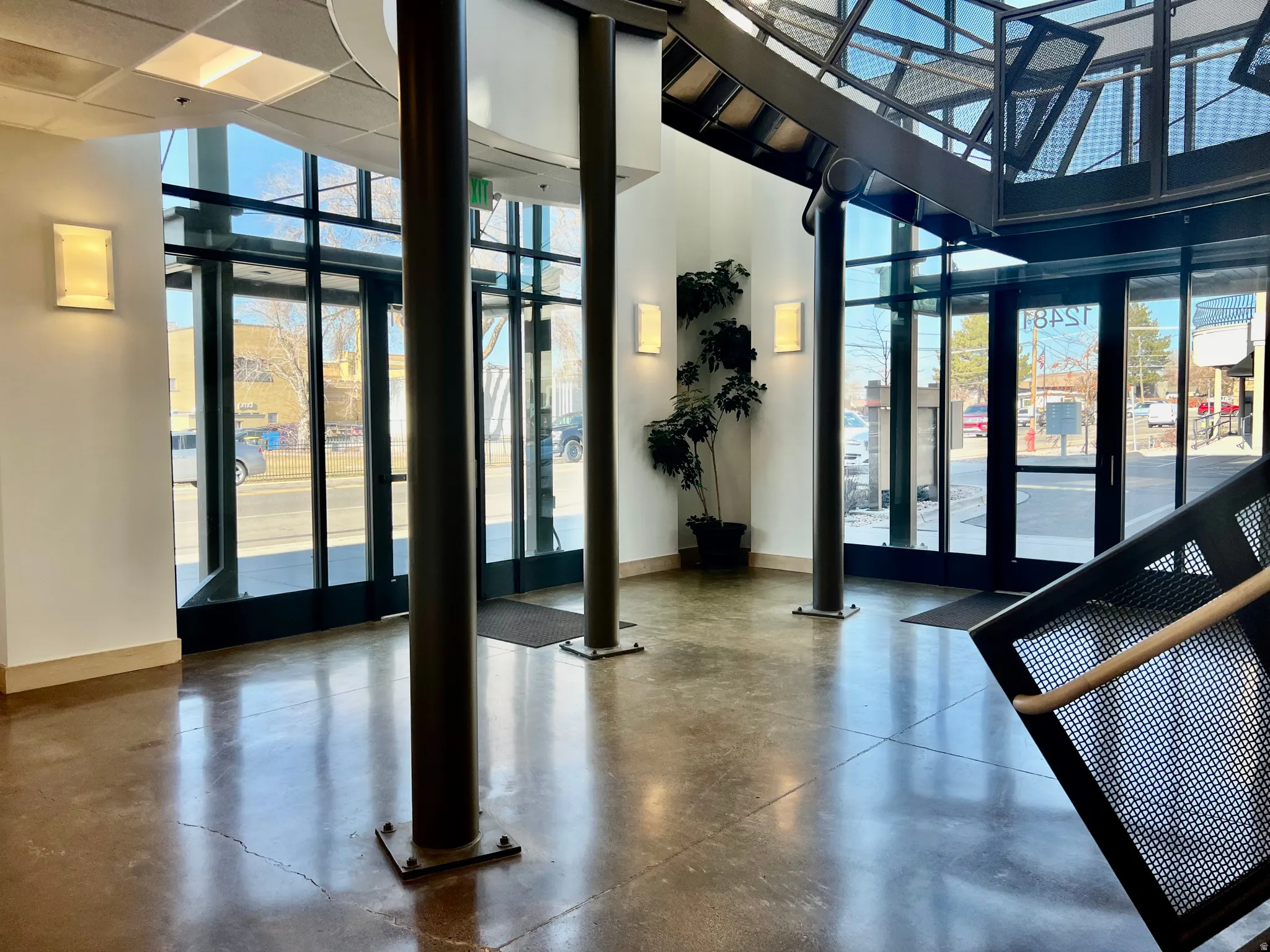 Contemporary entry featuring polished concrete flooring, extensive window walls, a striking industrial-style staircase with perforated metal panels, and integrated wall sconces