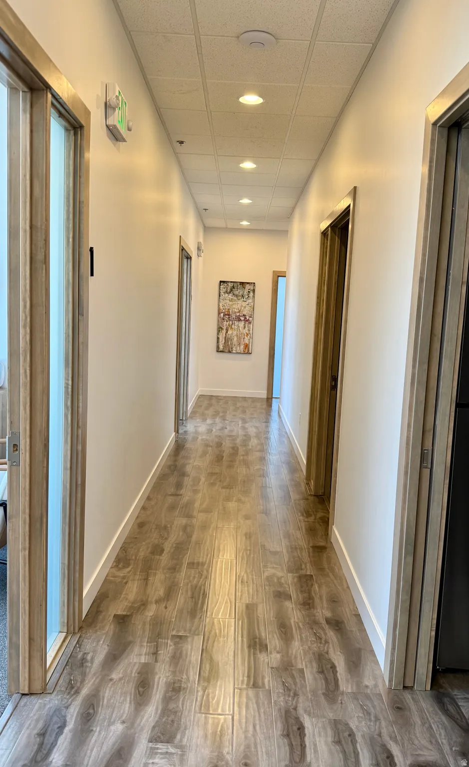 Hallway featuring wood-finish flooring, recessed ceiling lighting, and white baseboards