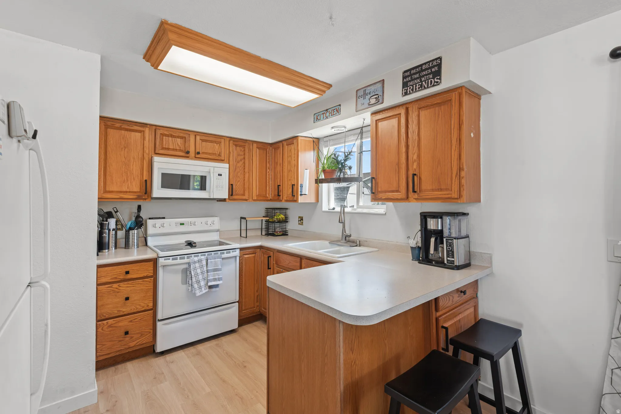 Kitchen featuring light wood-finish cabinetry, white appliances, light countertops, a double basin sink, and wood-finish flooring