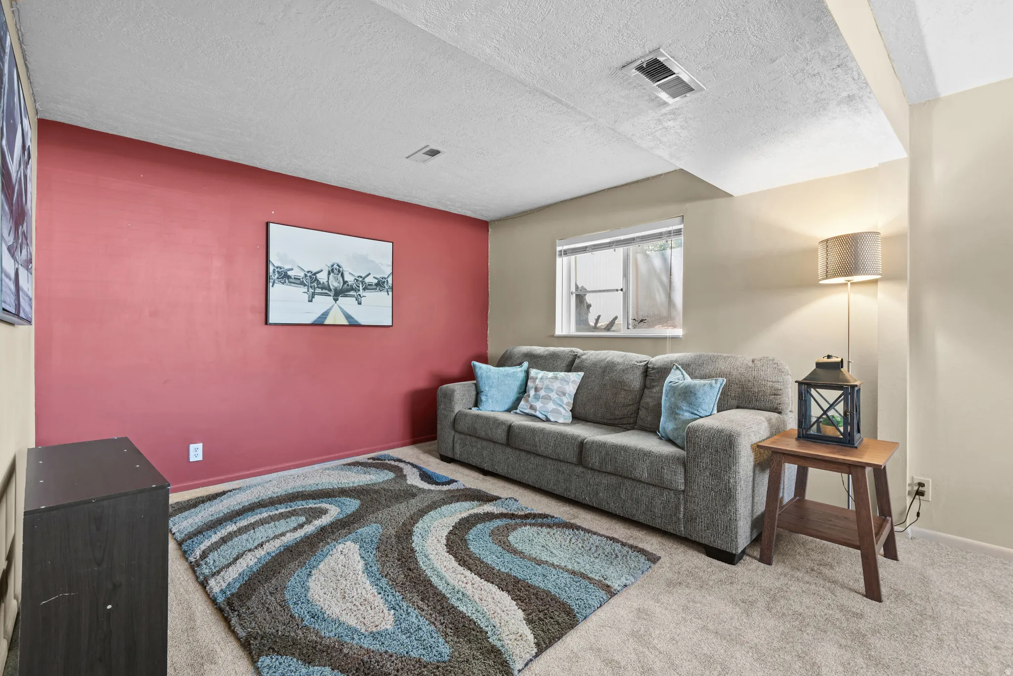 Carpeted room featuring a red accent wall, neutral painted walls, and a window providing natural light