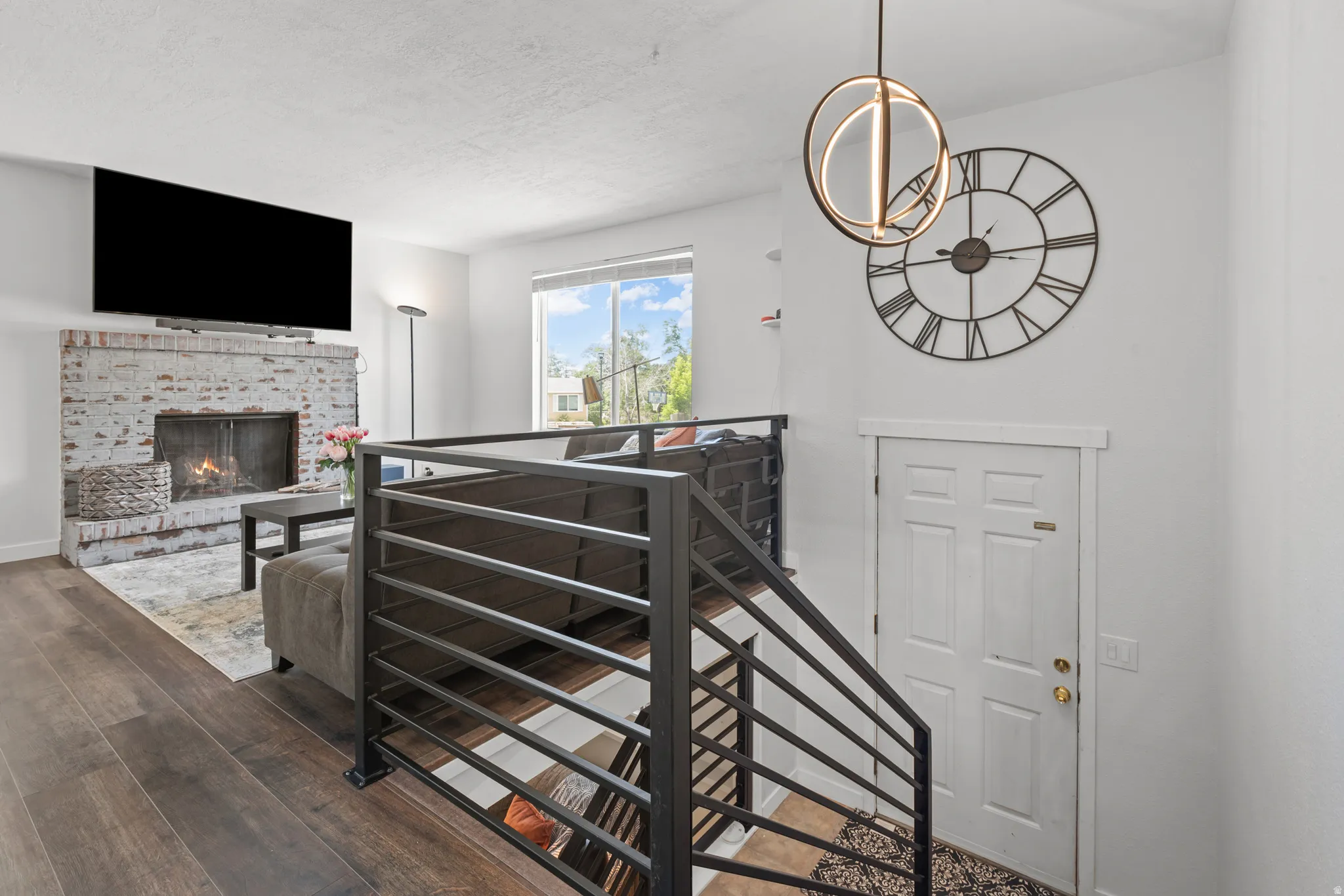 Living area featuring wood-finish flooring, a white-painted brick fireplace with a hearth, and a large window