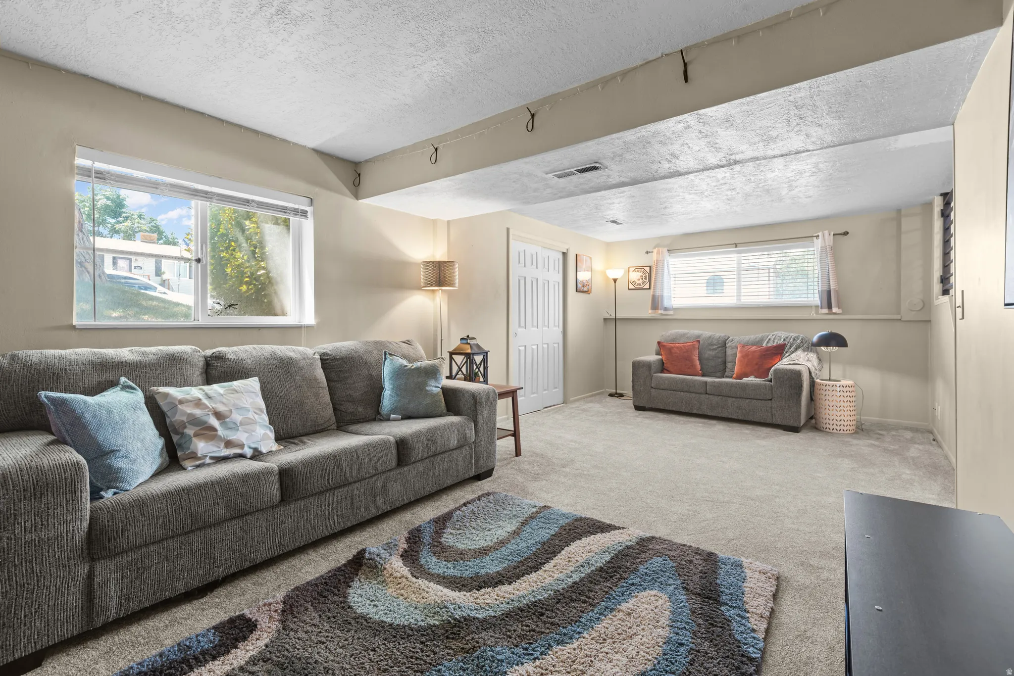Carpeted living space featuring neutral wall paint, two large windows with blinds, and white bi-fold doors