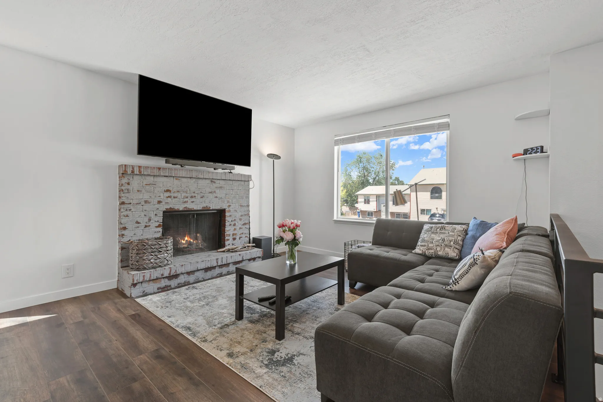 Living area featuring wood-finish flooring, a painted brick fireplace, a large picture window, and a built-in wall shelf