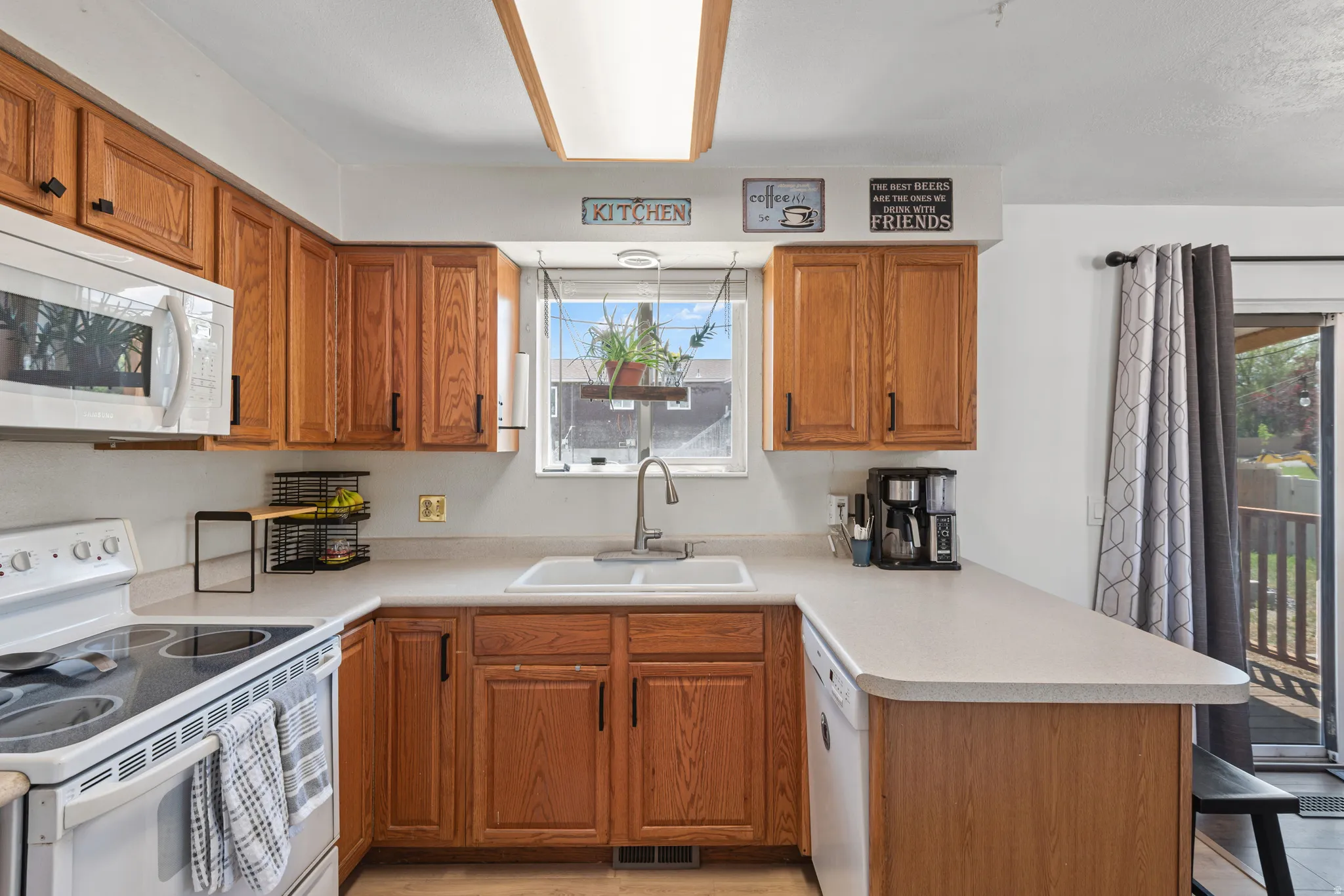 Kitchen featuring wood cabinetry, white countertops, built-in microwave, white electric range, and a single basin sink under a window