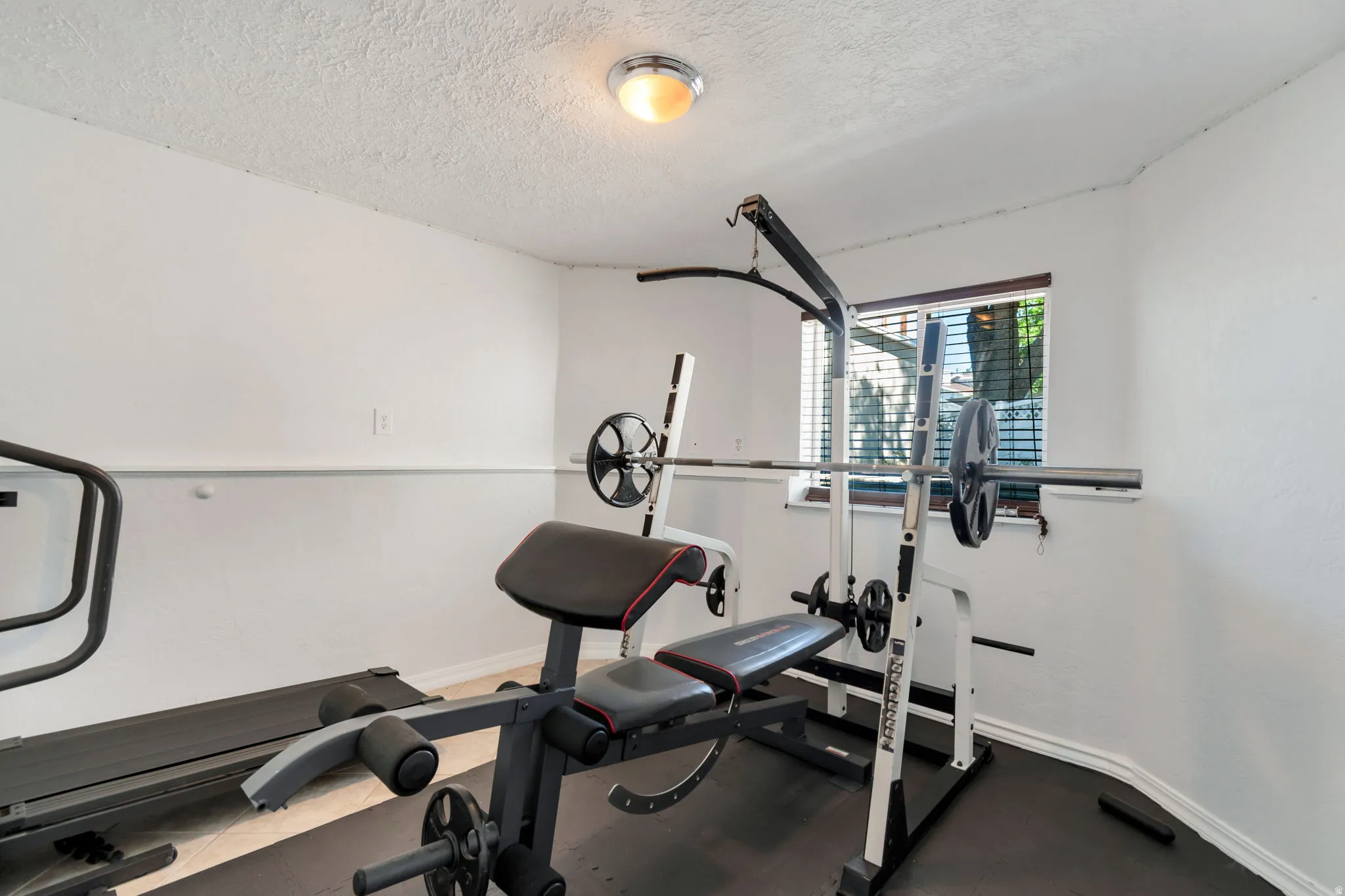 Dedicated room featuring a window with horizontal blinds, a ceiling-mounted light fixture, white walls, and a textured ceiling