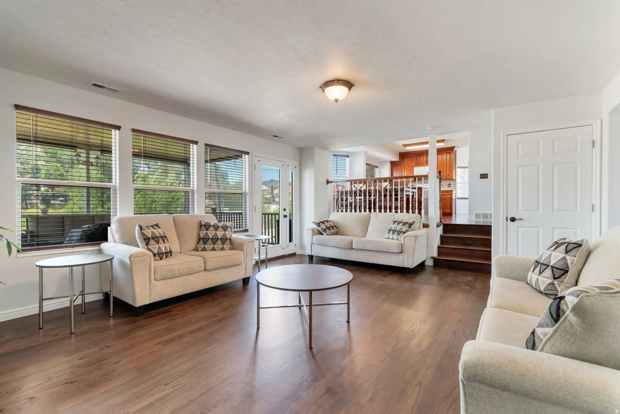 Spacious living area featuring wood-finish flooring, multiple large windows with blinds, and white trim