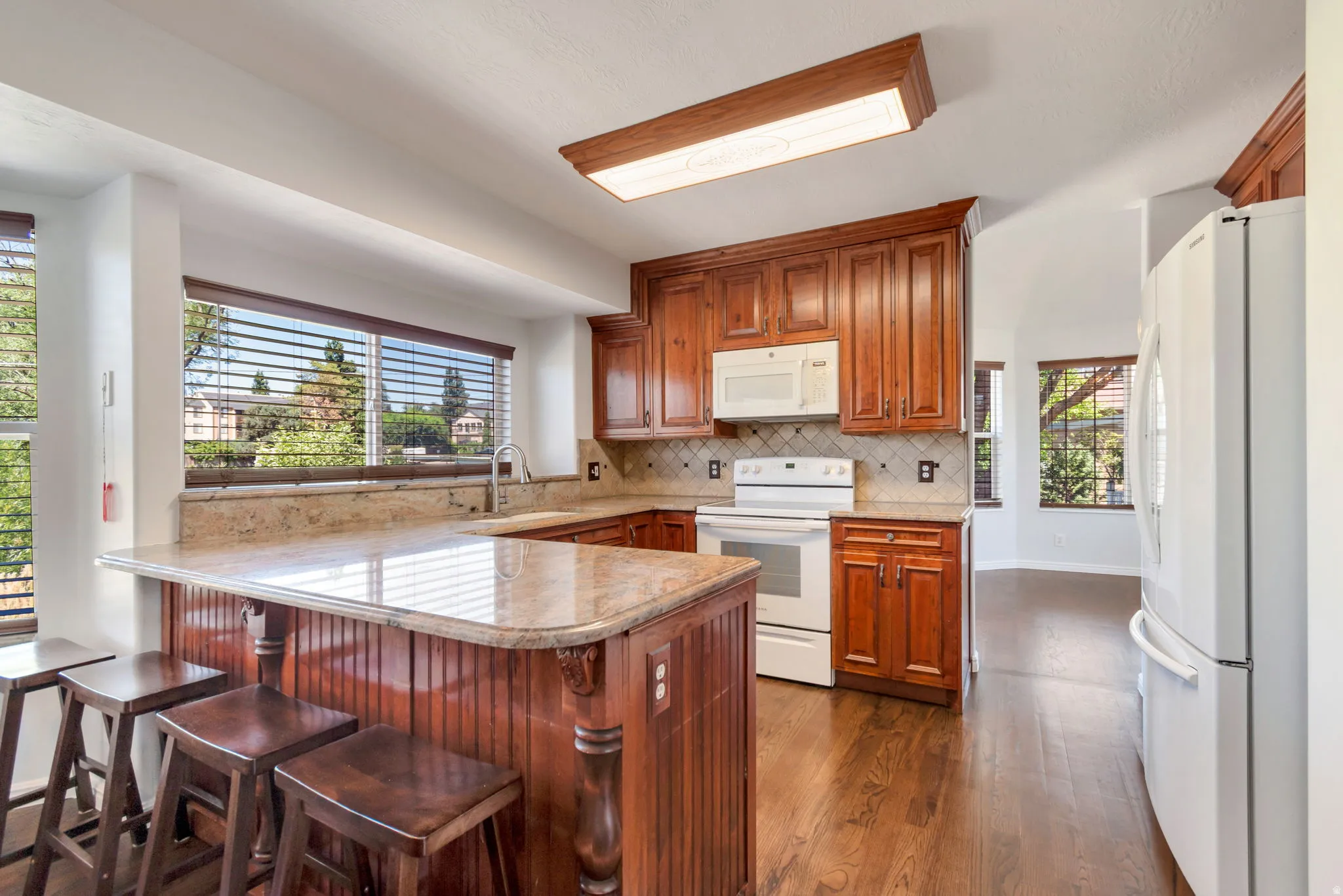 Kitchen featuring wood-finish flooring, rich wood cabinetry, light-toned countertops, and a white appliance suite