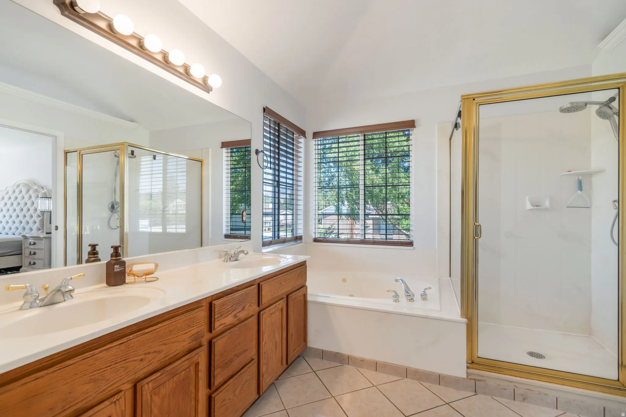 Bathroom featuring a dual vanity with wood cabinetry, a built-in jetted tub, and a separate shower enclosure with gold-toned framing