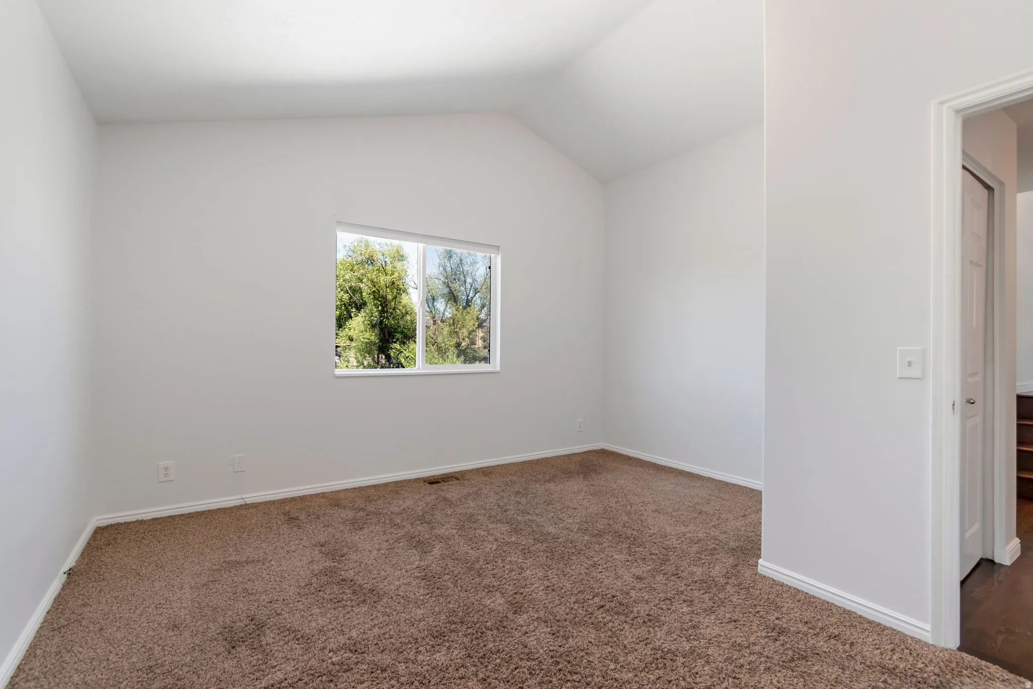 Bright interior space featuring a window, vaulted ceiling, and plush brown carpeting