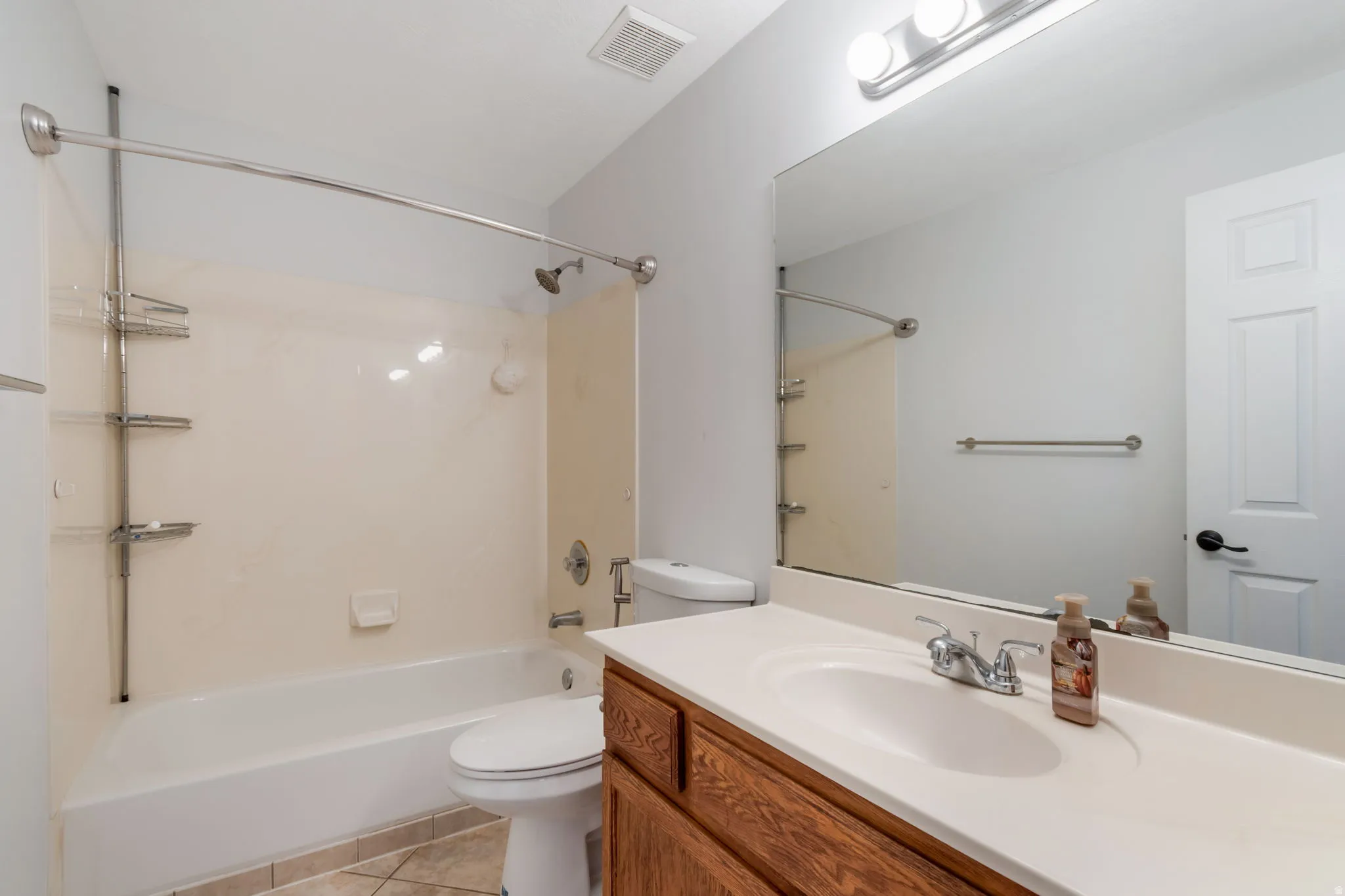 Bathroom featuring a combination shower and tub with a curved shower rod, a single vanity with a white countertop and wood-finish cabinetry, a large wall-mounted mirror, and tile flooring