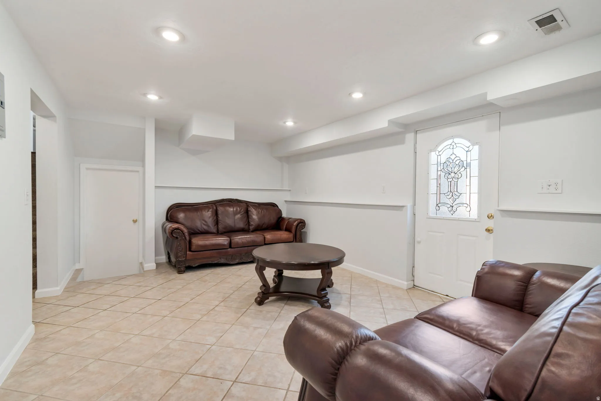 Recessed lighting illuminates this space featuring tile flooring and a white door with decorative glass