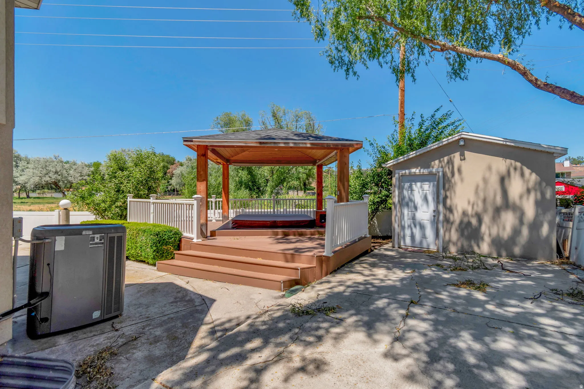 Backyard featuring a covered gazebo with a built-in spa, a multi-tiered deck with white railings, and an stucco outbuilding with a white door
