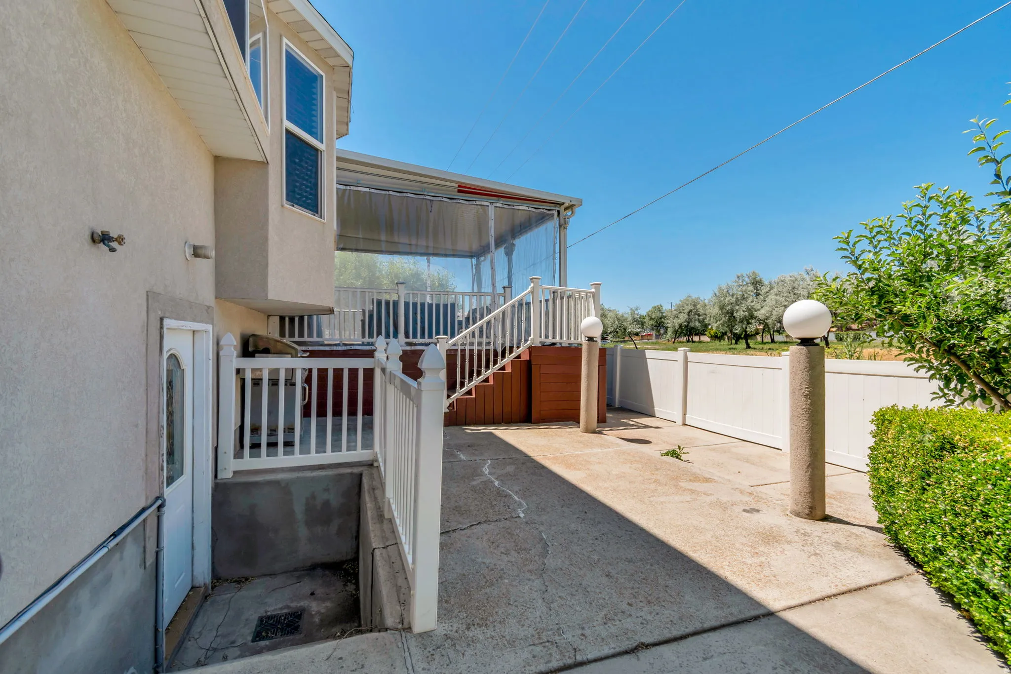 Spacious concrete patio featuring access to a lower-level entry, a white railing leading to an elevated deck, and a privacy fence