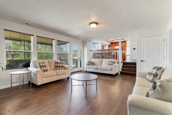 Spacious living area featuring wood-finish flooring, multiple large windows with blinds, and white trim