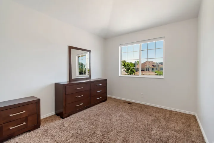 Bedroom featuring a large grid-patterned window, light-colored walls, and textured carpet flooring