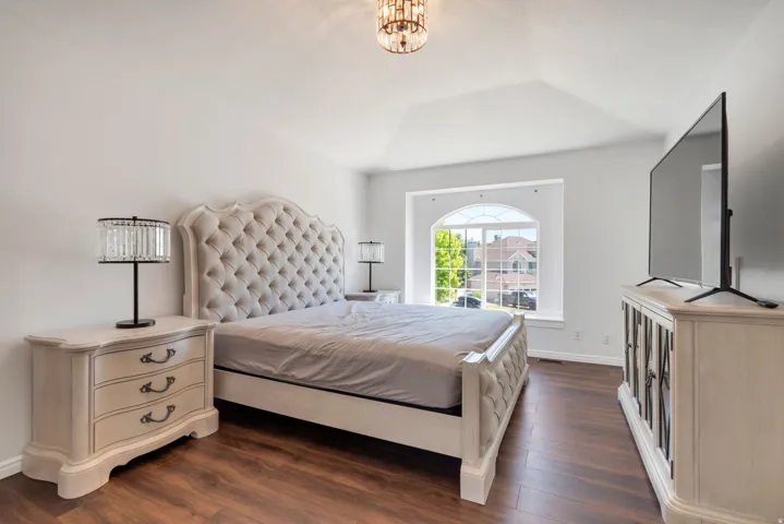 Vaulted ceiling bedroom featuring wood-finish flooring, a large arched window, and a decorative ceiling light fixture