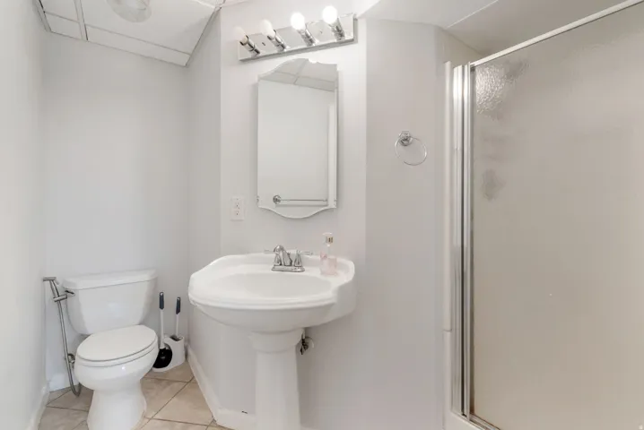 Bathroom featuring a pedestal sink, wall-mounted mirror, and a shower enclosure with a clear door