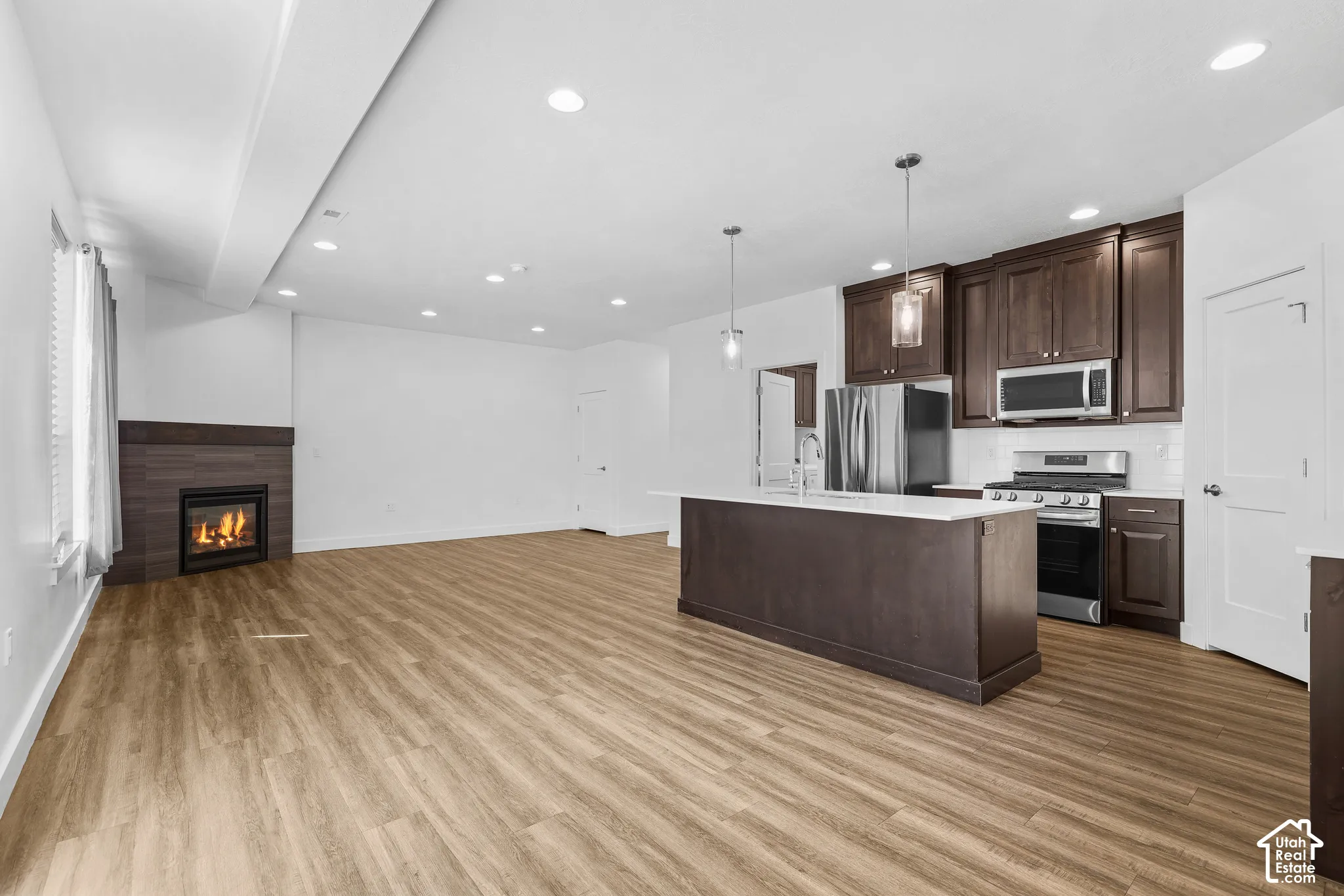 Open-concept living space featuring wood-finish flooring, a contemporary fireplace with a dark wood mantel, and recessed lighting