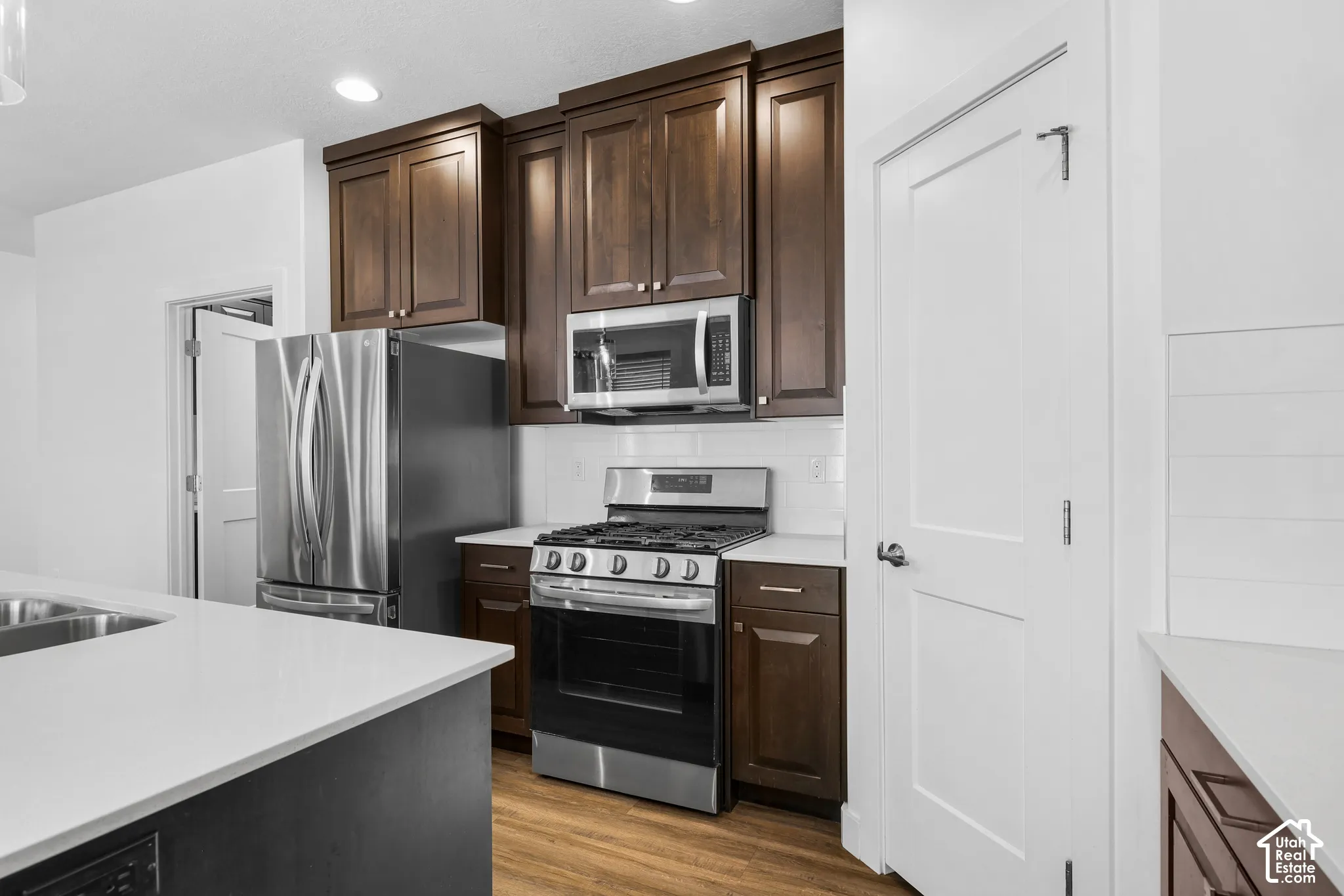 Kitchen featuring dark wood cabinetry, white countertops, stainless steel appliances, white subway tile backsplash, and wood-finish flooring
