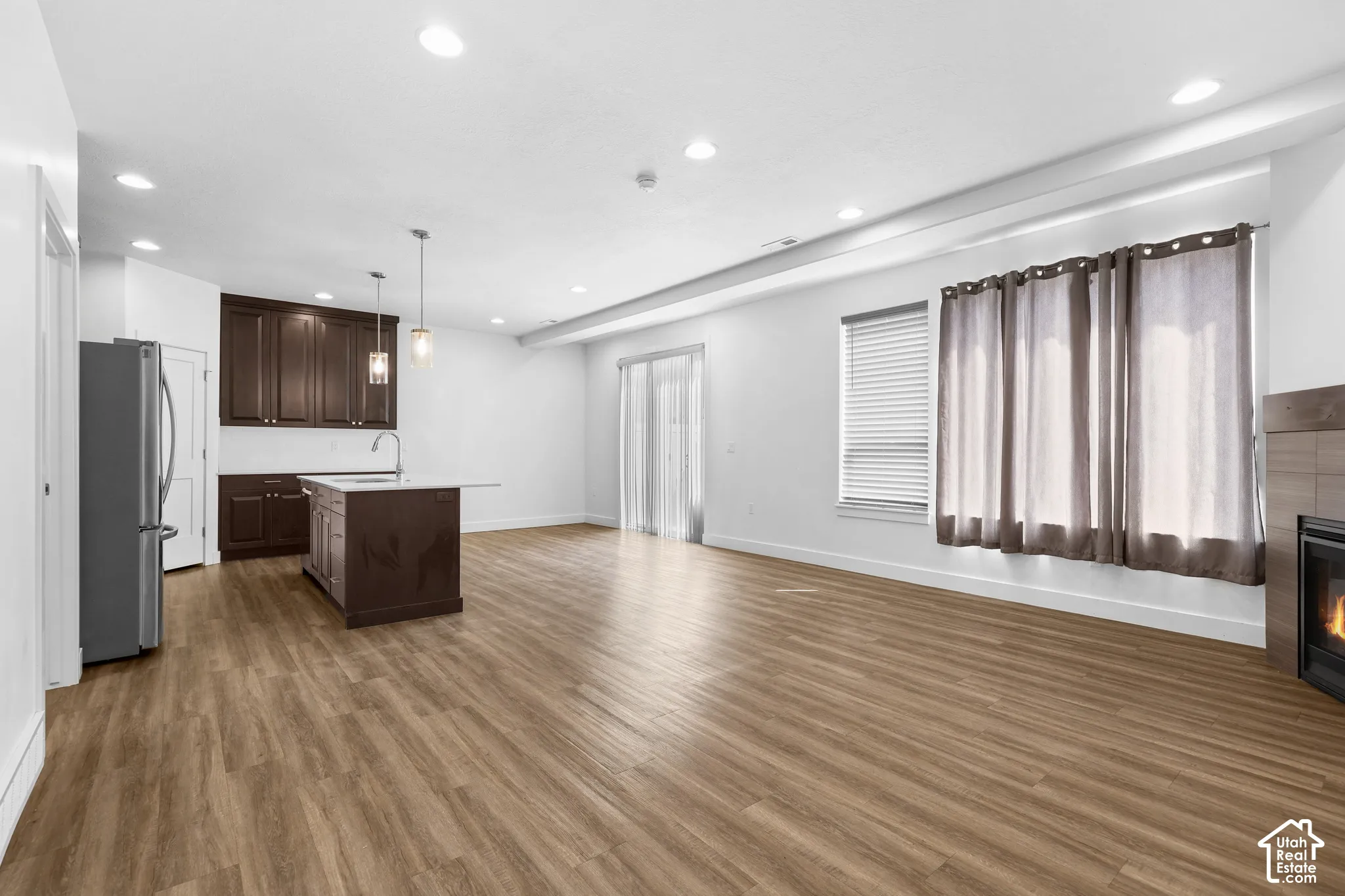 Open-concept living area featuring wood-finish flooring, a kitchen island with pendant lighting, stainless steel refrigerator, and built-in fireplace
