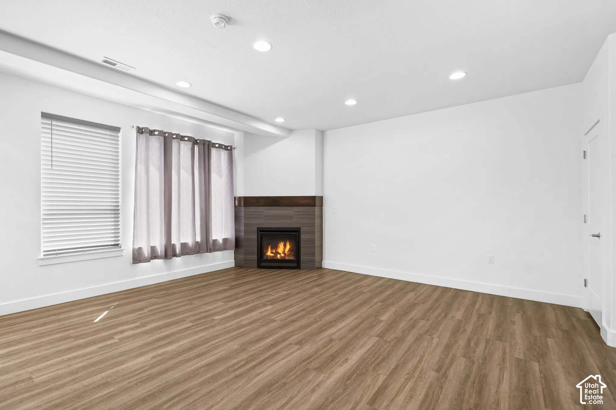 Wood-finish flooring, recessed lighting, and a corner fireplace with a dark tile surround