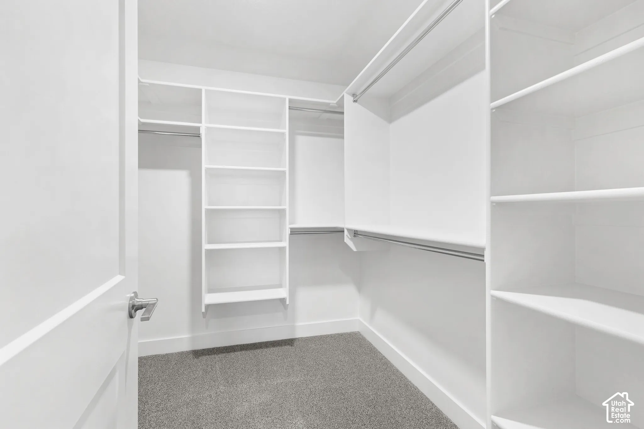 Walk-in closet with built-in white shelving, multiple hanging rods, and gray carpet flooring