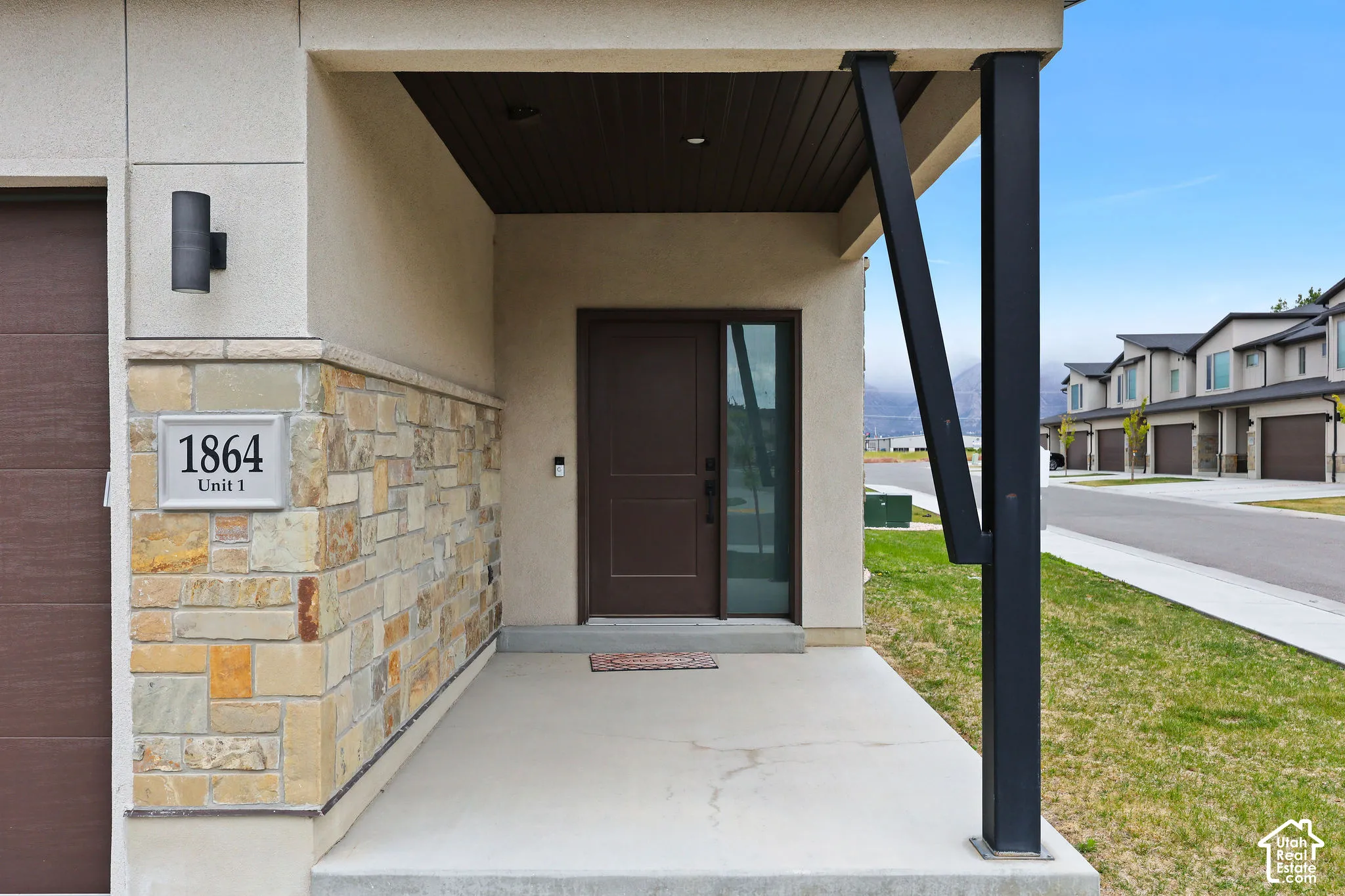 Covered entryway featuring a stone veneer accent wall, contemporary exterior lighting, a dark-stained solid front door with a sidelight, and a concrete porch with a dark-finished support beam