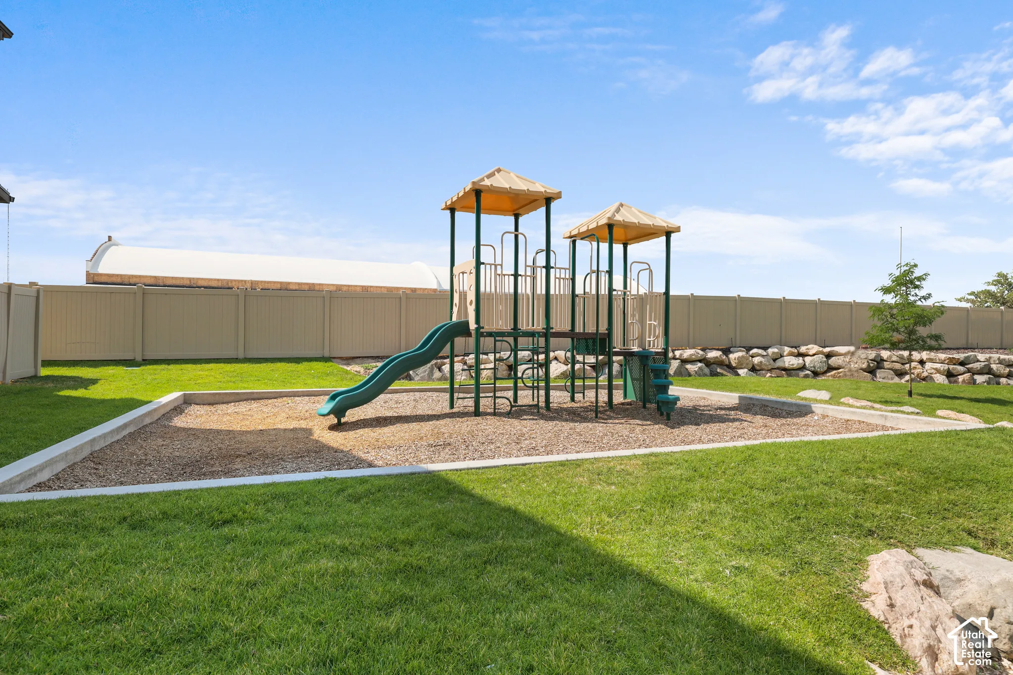 Backyard recreation area featuring a playground structure with slide, a rock retaining wall, and a full privacy fence