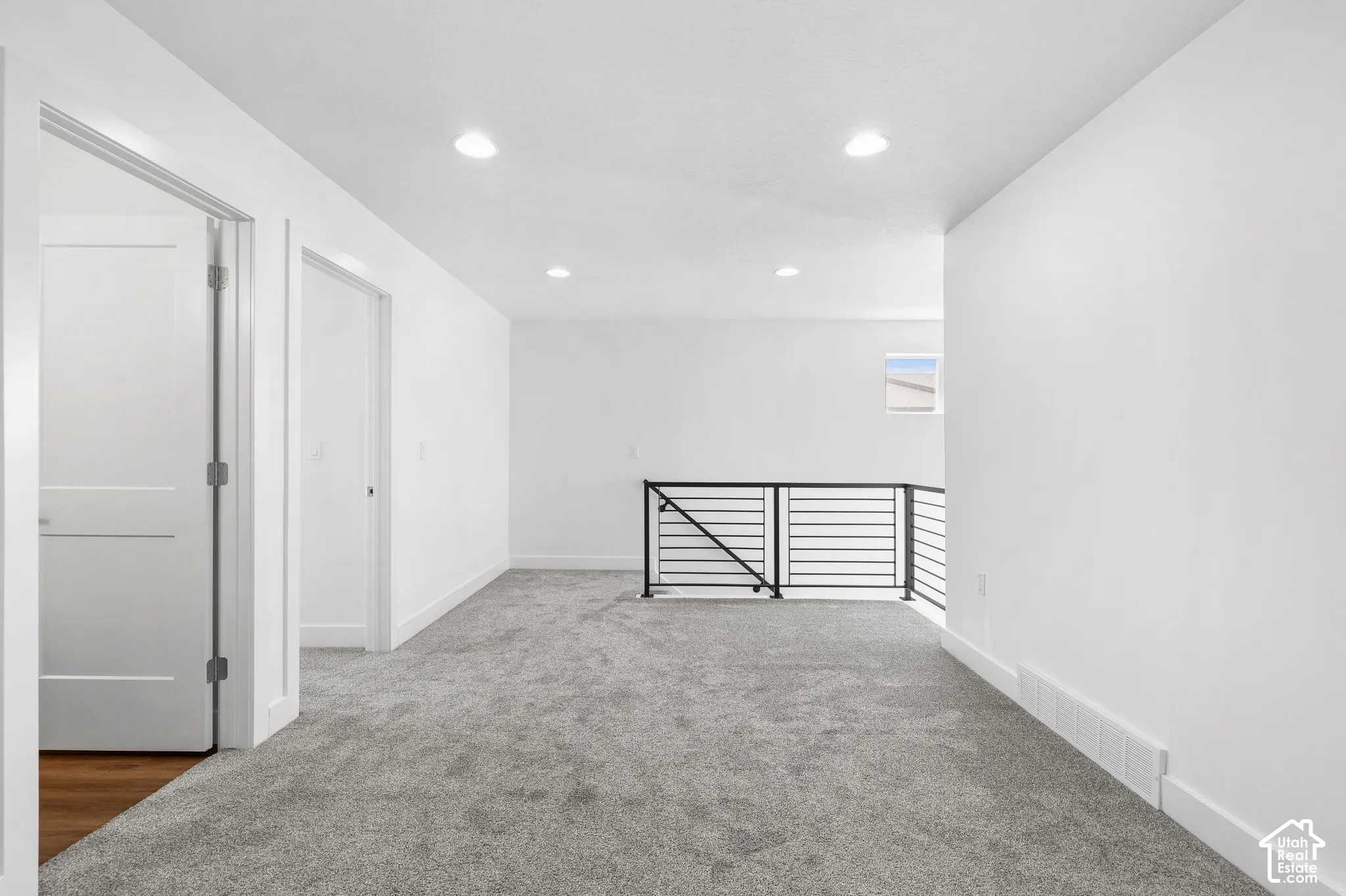 Spacious landing with neutral carpeting, recessed lighting, and modern black railing
