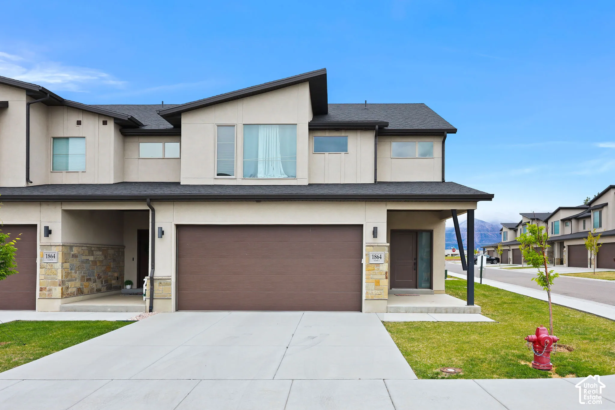 Contemporary townhouse exterior featuring a two-car garage, stone facade accents, and a covered entryway